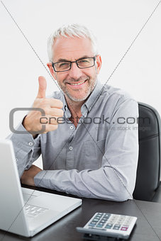Smiling businessman with laptop gesturing thumbs up