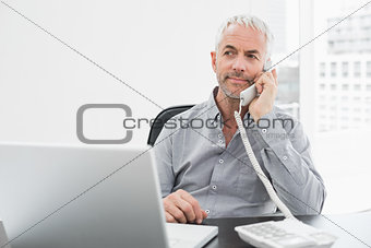 Businessman on call in front of laptop at office desk