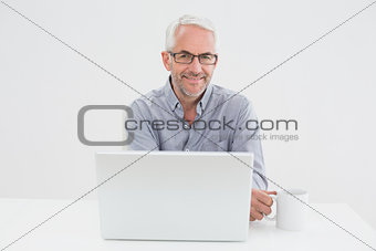 Smiling mature businessman with laptop and coffee cup