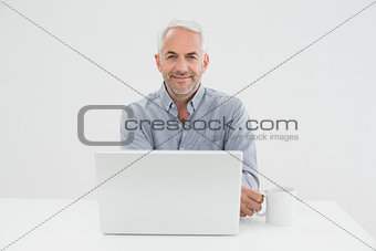 Smiling mature businessman with laptop and coffee cup