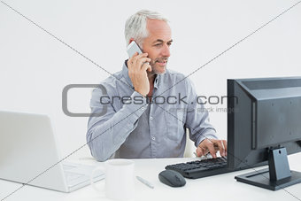 Businessman with cellphone, laptop and computer at desk