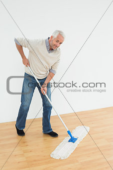 Full length portrait of a smiling mature man mopping the floor
