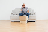 Mature man using cellpone on sofa with boxes in a house