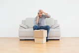 Annoyed man using cellpone on sofa with boxes in house