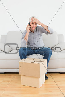 Annoyed man using cellpone on sofa with boxes in a new house