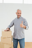 Smiling man with boxes gesturing thumbs up in a new house