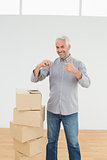 Man with boxes and keys gesturing thumbs up in a new house