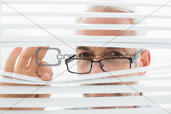 Serious mature businessman peeking through blinds