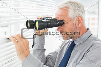 Businessman peeking with binoculars through blinds