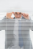 Portrait of a businessman peeking through blinds in office