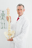 Confident doctor holding skeleton model in office