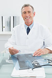 Smiling male doctor sitting at desk in office