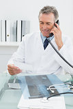 Doctor using telephone while looking at note in office