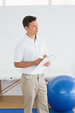 Thoughtful trainer with clipboard in gym at hospital