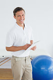 Smiling male trainer with clipboard in gym at hospital