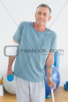 Smiling mature man with crutch and dumbbell