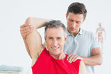 Physiotherapist stretching a smiling mature mans arm