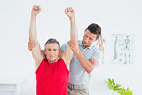Physiotherapist stretching a mature mans arms
