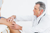 Side view of a mature doctor examining patients knee