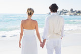 Bride and groom holding hands looking out to sea