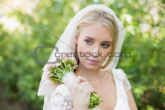 Peaceful bride holding her bouquet wearing a veil