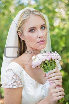 Peaceful bride holding her bouquet wearing a veil looking at camera