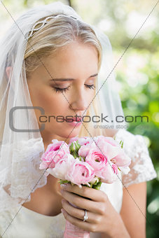 Happy bride in a veil smelling her rose bouquet