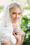 Blonde smiling bride in a veil holding her hands to her chest