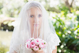 Smiling bride wearing veil over face holding rose bouquet