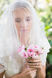 Calm bride wearing veil over face holding rose bouquet