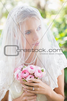 Content bride wearing veil over face holding rose bouquet