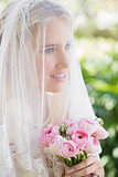 Happy bride wearing veil over face holding rose bouquet