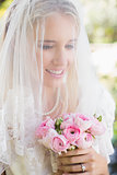Smiling bride wearing veil over face holding bouquet