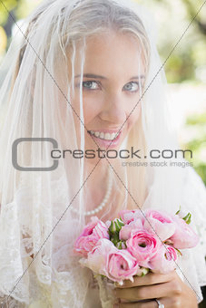 Smiling bride wearing veil over face holding bouquet looking at camera