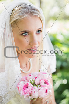 Happy bride wearing veil holding bouquet looking away