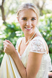 Smiling blonde bride holding her dress looking at camera