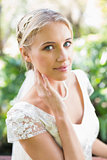 Smiling blonde bride in pearl necklace touching her face
