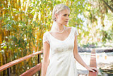 Smiling blonde bride in pearl necklace standing on a bridge