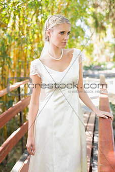 Content blonde bride in pearl necklace standing on a bridge