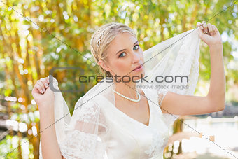 Pretty content blonde bride holding her veil out smiling at camera