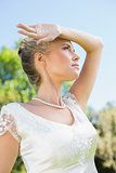 Pretty blonde bride holding arm to forehead on sunny day