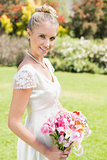 Pretty blonde bride holding lily bouquet smiling at camera