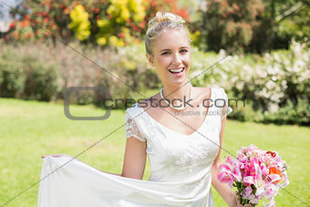 Beautiful blonde bride holding bouquet and her dress smiling at camera