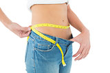 Mid section of woman measuring waist in a big sized jeans