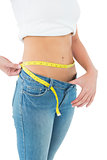 Mid section of a woman measuring waist in a big sized jeans
