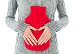 Mid section of a woman holding red hot water bag on abdomen
