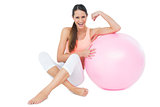 Cheerful fit woman flexing muscles  by fitness ball