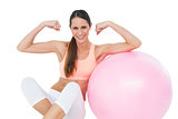 Cheerful fit woman flexing muscles  by fitness ball