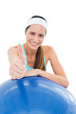 Smiling fit woman with fitness ball gesturing thumbs up