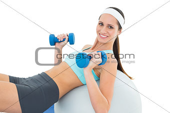 Smiling fit woman exercising with dumbbells on fitness ball